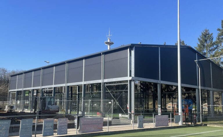 Buitenaanzicht van padelhal met vaste lichtdoorlatende schermen die regeninval beperken