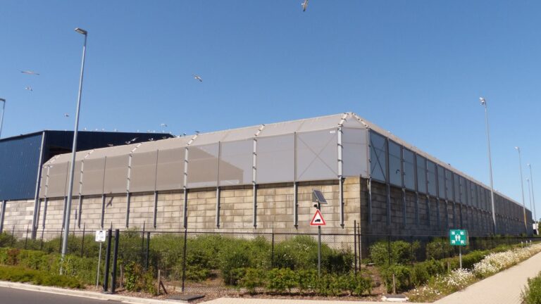 Stofmuur bij buitenopslag op recyclage site met houtschredder